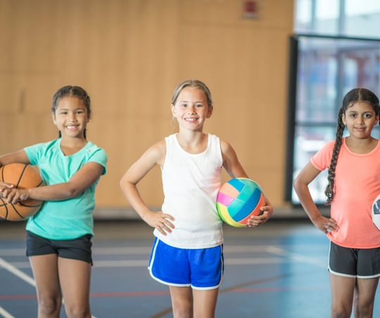 Three Young Girls Holding Different Balls For Basketball, Volleyball, And Soccer