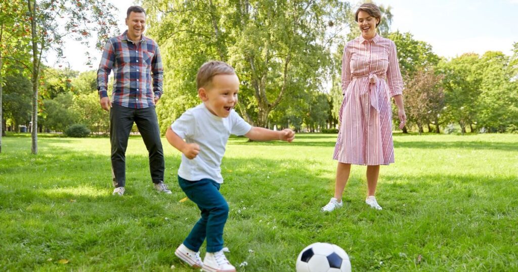 child playing soccer while both parents watch on